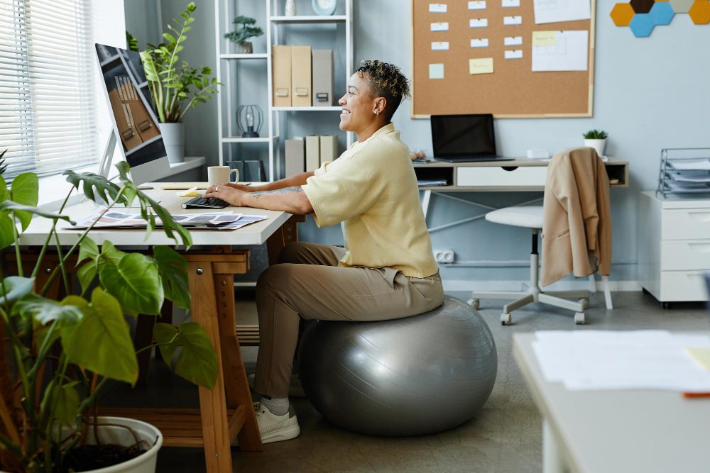 Portrait de profil d'une jeune femme assise sur un ballon de fitness sur son lieu de travail